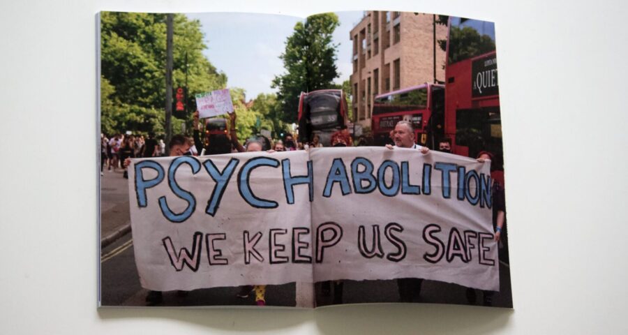 The image shows a photograph of a protest. The people at the front of the protest are holding a painted sheet which reads 'Psych abolition. We keep us safe'