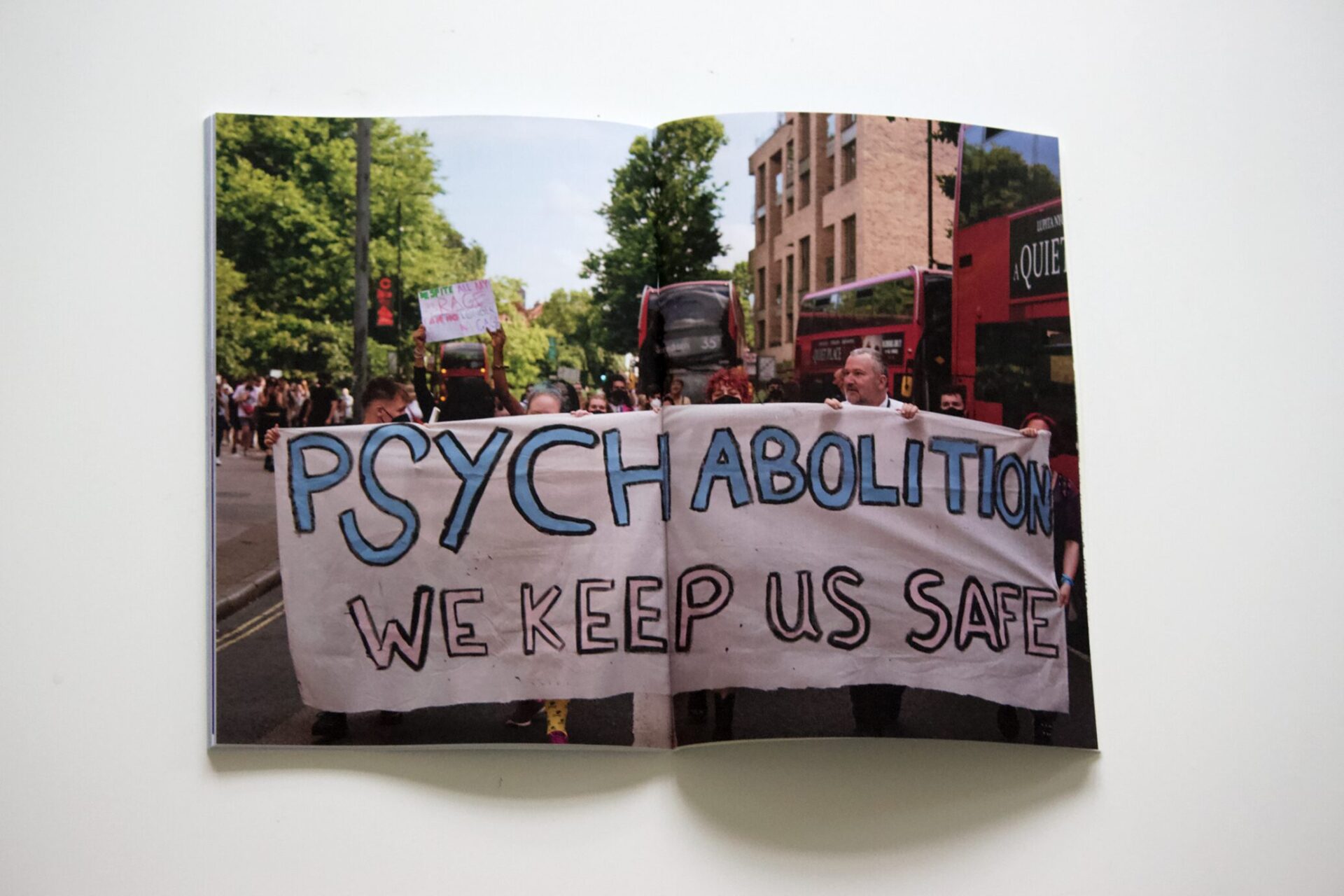 The image shows a photograph of a protest. The people at the front of the protest are holding a painted sheet which reads 'Psych abolition. We keep us safe'